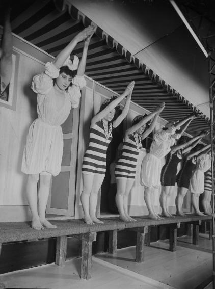 Fotografi af kvinder, der står med armene over hovedet, som om de skal lave et hovedspring.