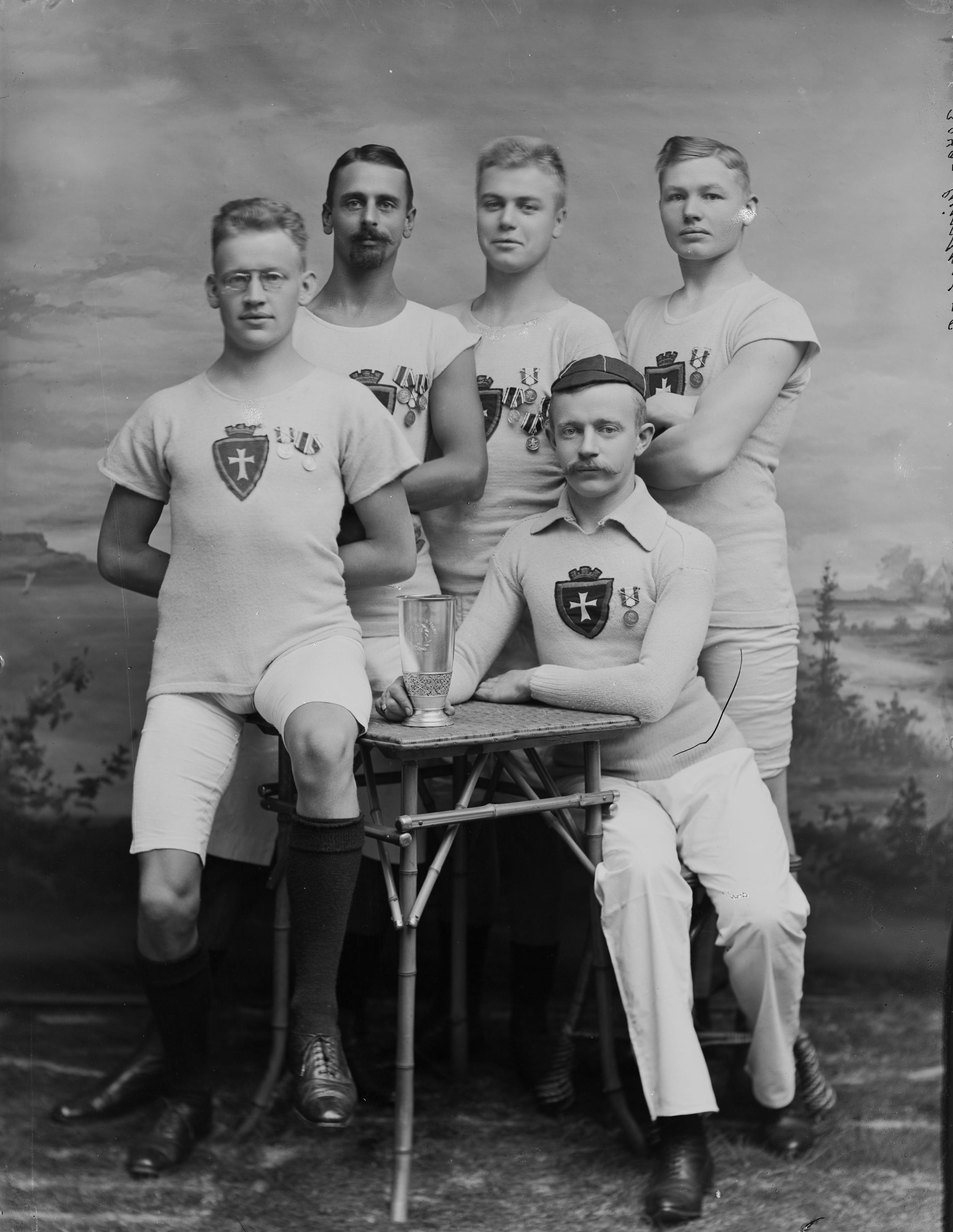 Fem atleter klædt i hvidt poserer med præmier på brystet