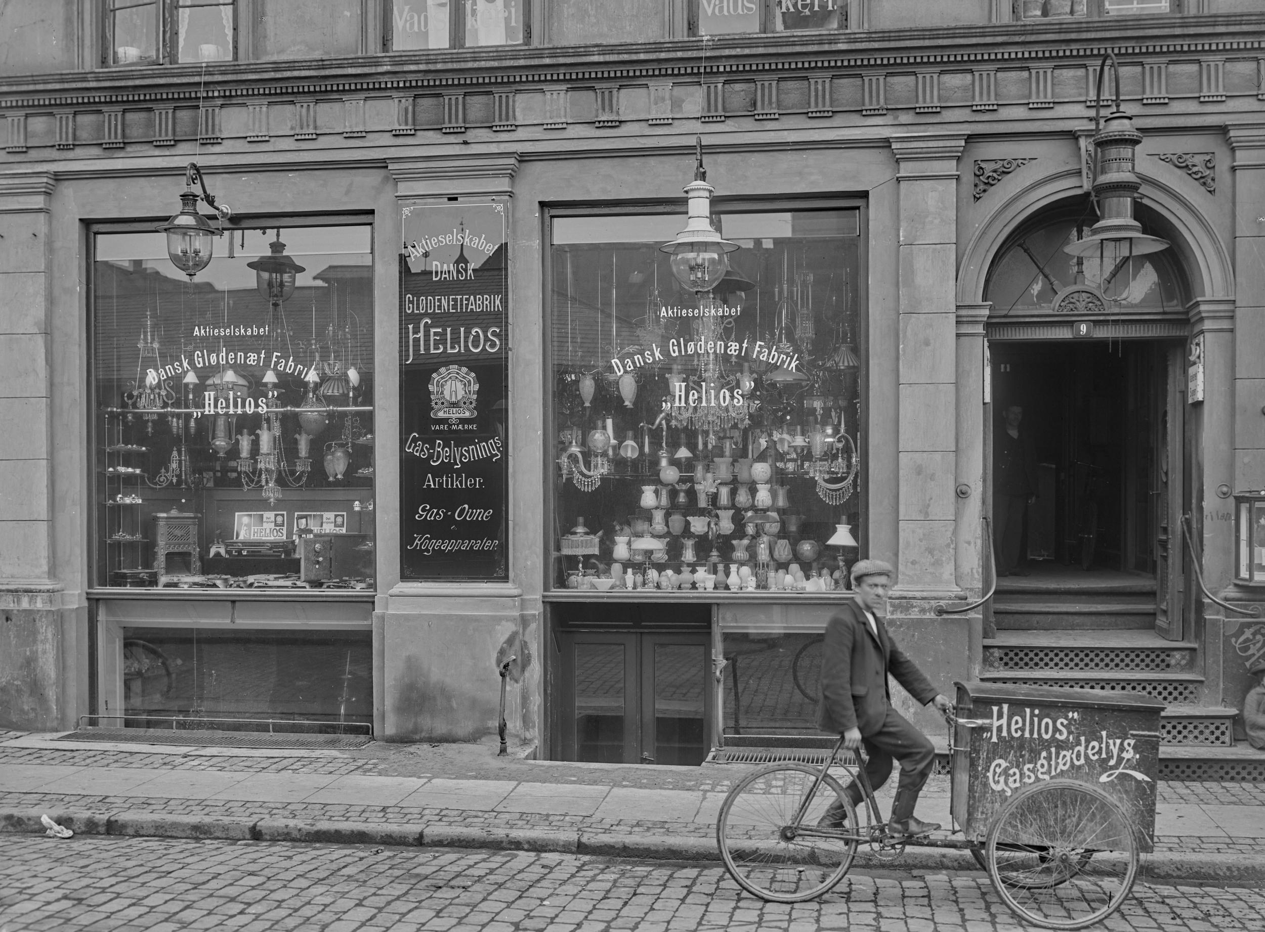 Flot butiksfacade med store vinduer. Foran butikken er en mand på cykel.