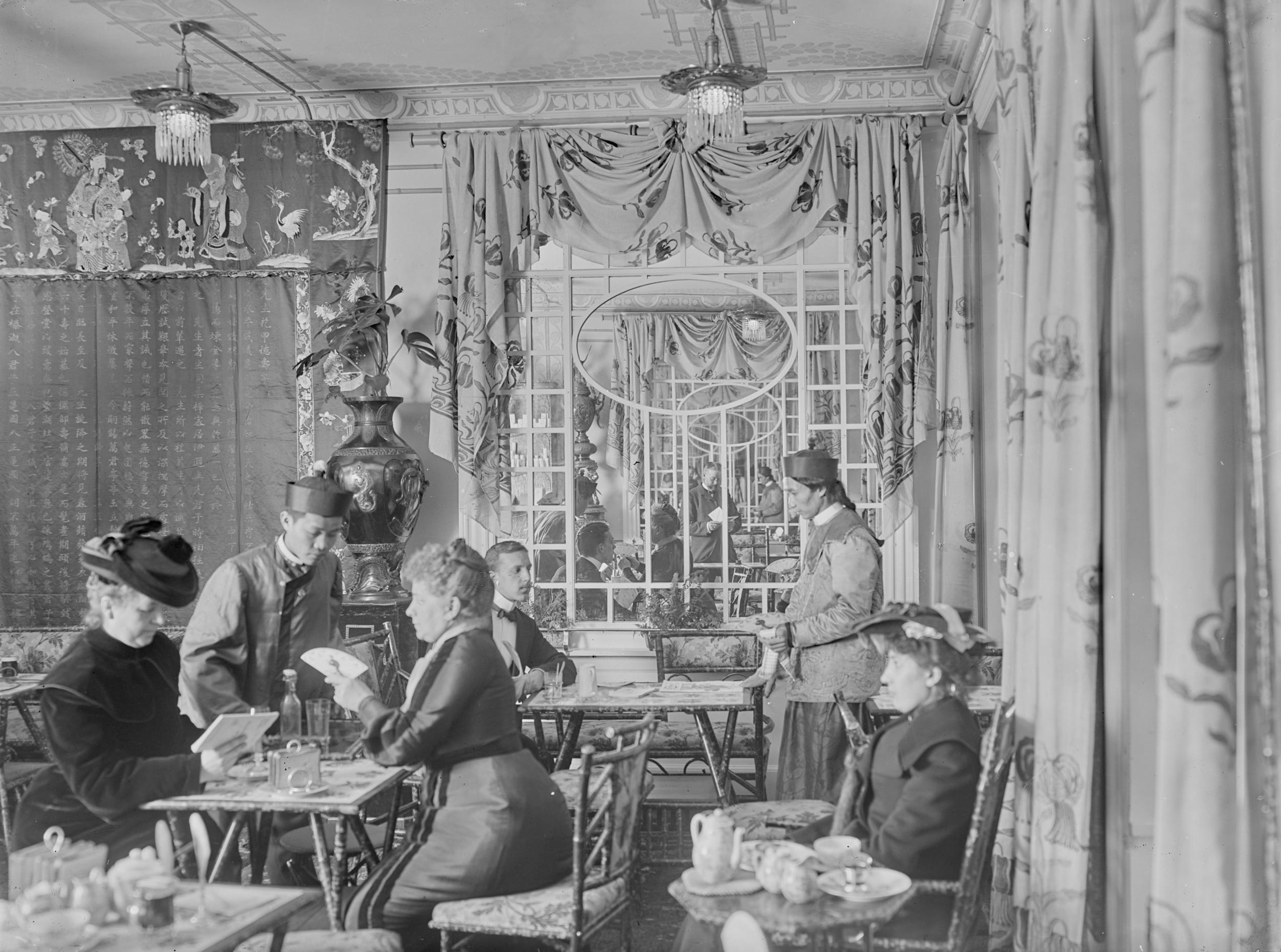 Fint klædte damer bliver betjent af kinesiske tjenere i en thesalon