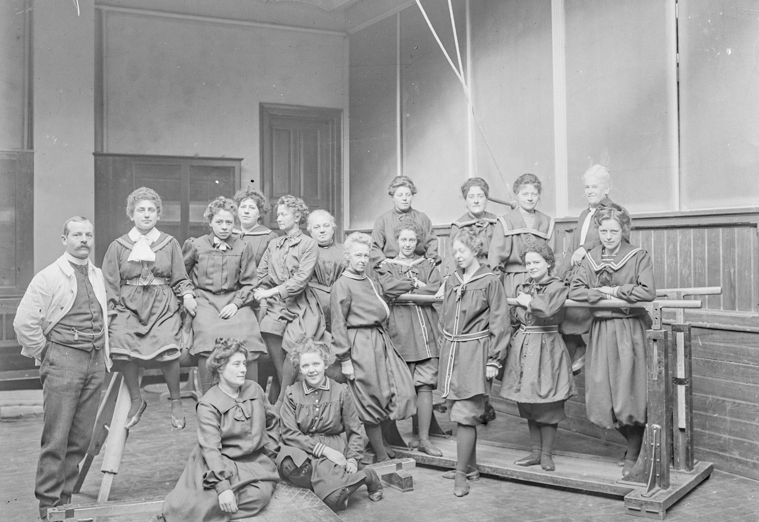 Fotografi af en gruppe kvinder iført datidens gymnastikdragt i en gymnastiksal.