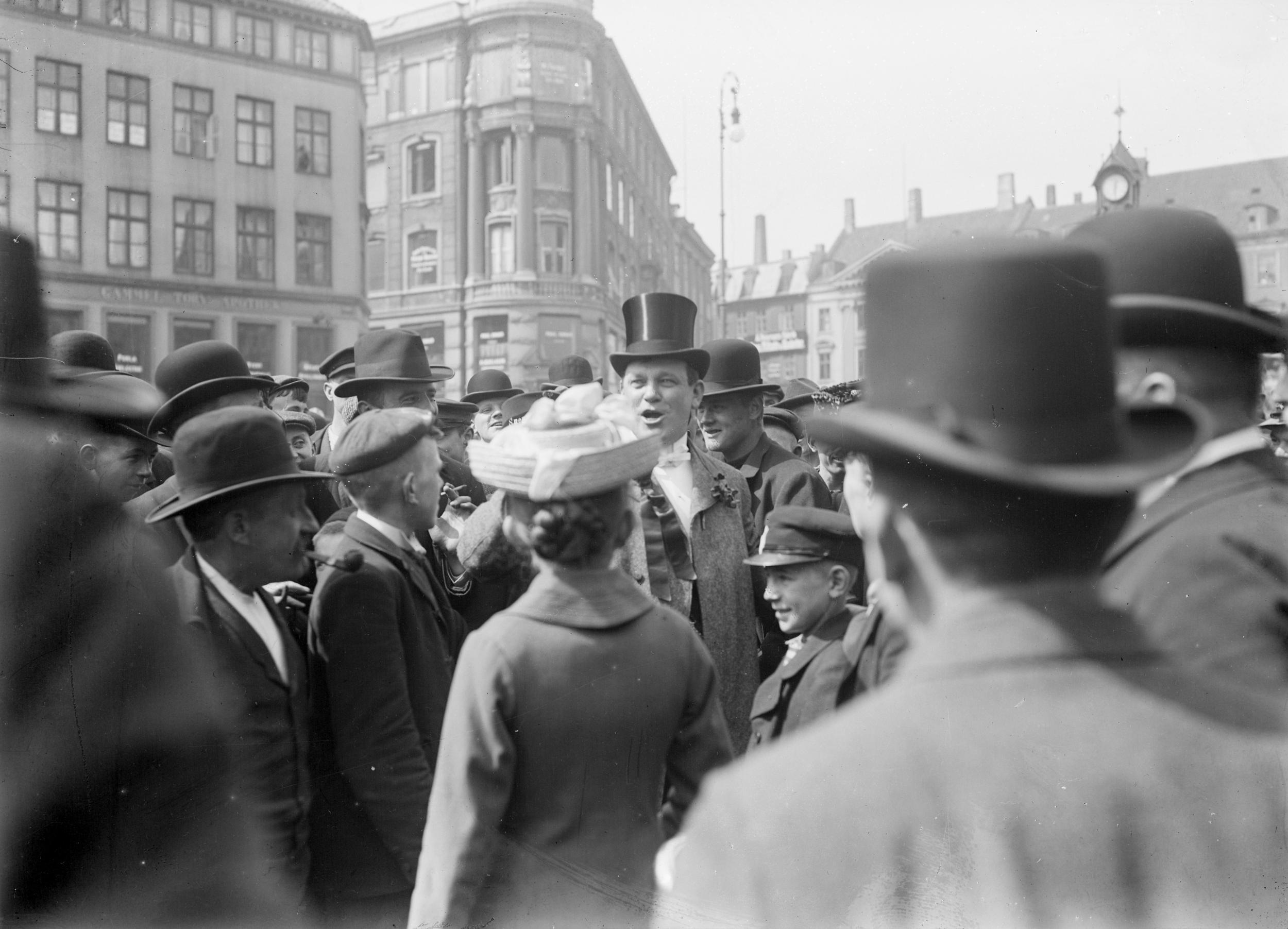 En mand i tophat står centreret i billedet, omringet af mennesker