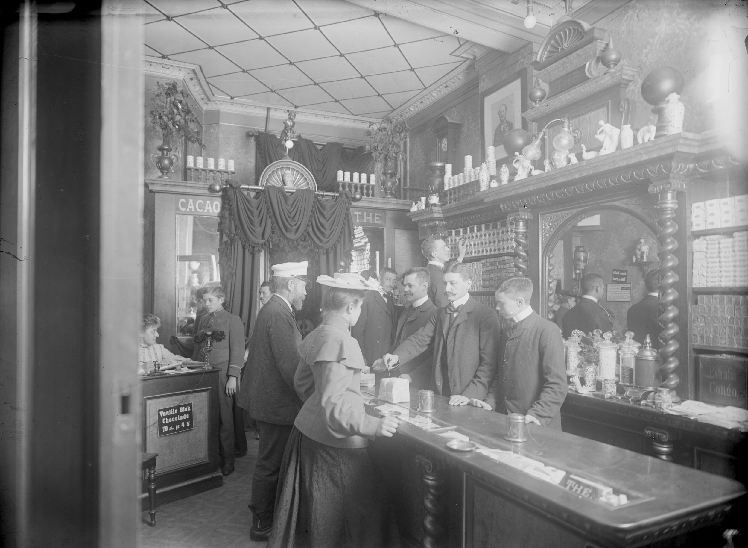 Indenfor i en kaffehandel. To kunder bliver betjent af tre mænd bag en skranke