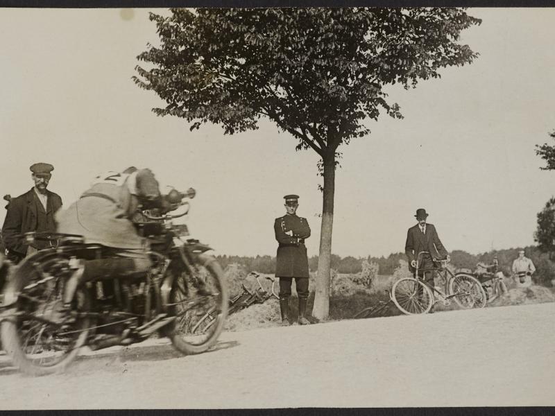 Mænd står på en vej og ser på en motorcykel med sidevogn køre forbi