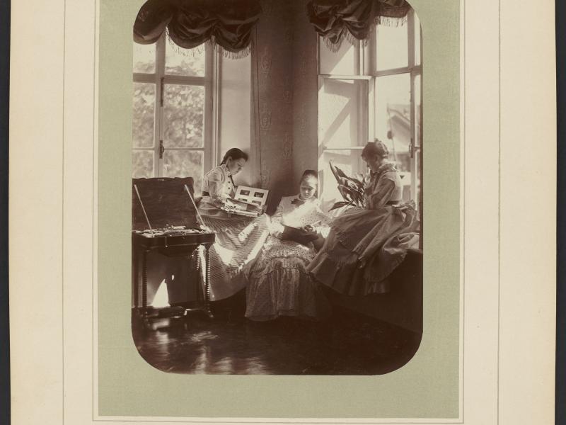 Tre kvinder sidder ved to store vinduer med fotoalbums i hænderne