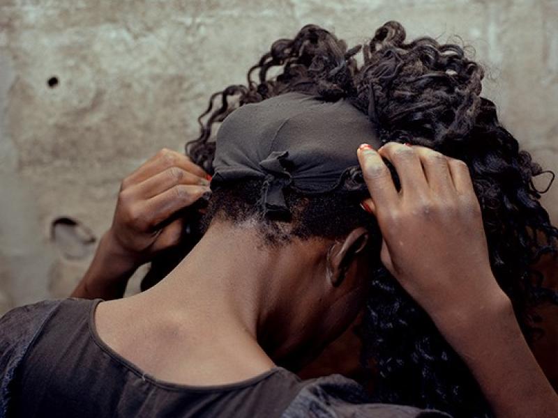 En sort kvindes baghoved mens hun sætter en paryk på