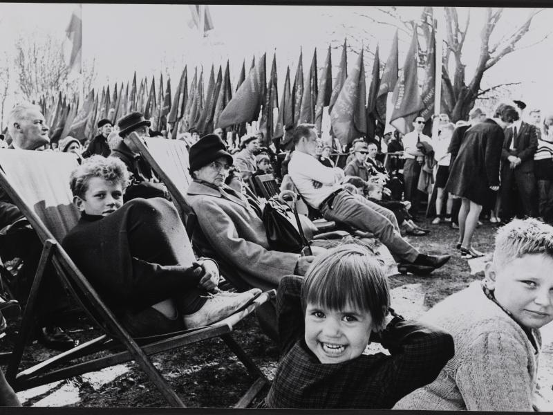 En gruppe mennesker sidder i stole foran en række af faner. Tre drenge i forgrunden smiler til kameraet.