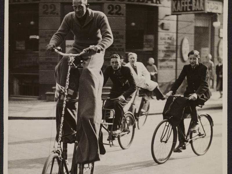 Tre mænd på cykler. Den forreste mand cykler på en væltepeter.