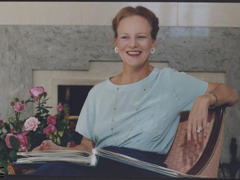 Farvebillede af Dronning Margrethe II, der sidder med en bog i skødet.