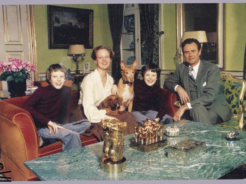 Dronning Margrethe II, prins Henrik, Kronprins Frederik og prins Joachim sidder i en sofa med deres hunde.