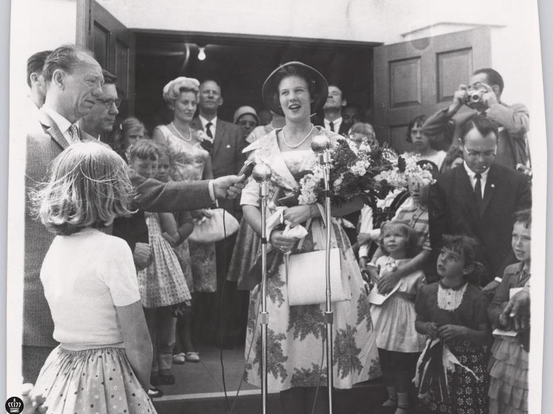 Dronning Margrethe II holder tale med publikum rundt om sig. Hun står med blomster.