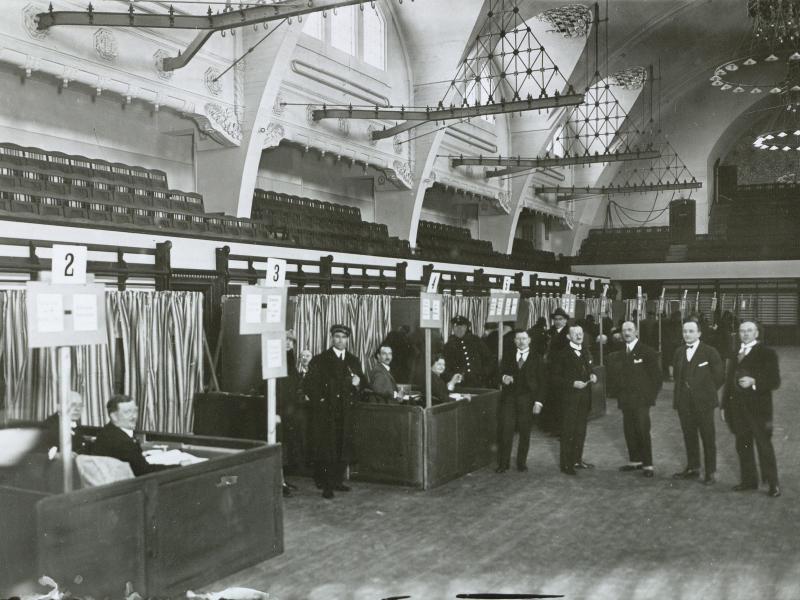 Mænd i jakkesæt står i afstemningslokale i gymnastiksal 2. dec. 1926