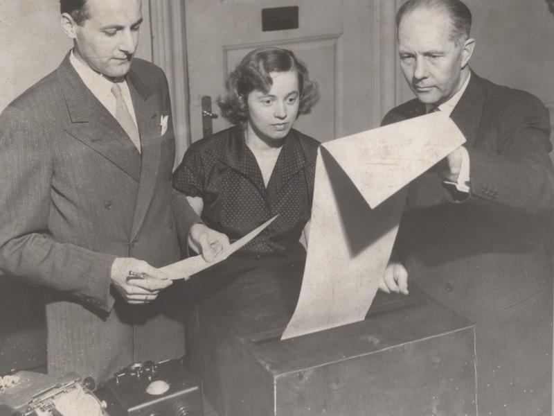A woman and two men look at the election results, which arrive on teleprinter at the Ministry of the Interior's Election Office