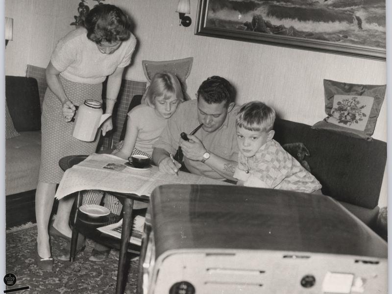 Familie sidder foran TV'et og kigger i avis
