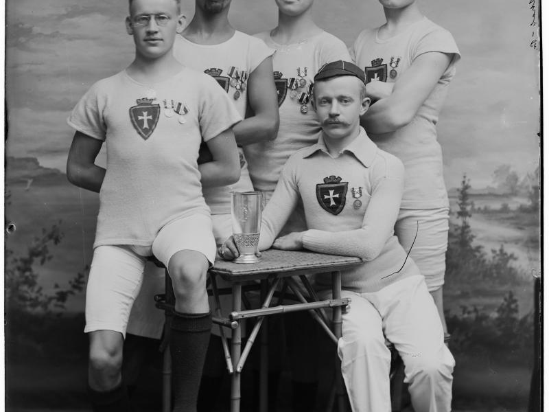 Fem atleter klædt i hvidt poserer med præmier på brystet