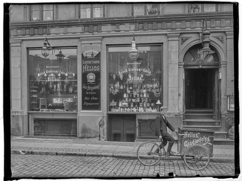 Flot butiksfacade med store vinduer. Foran butikken er en mand på cykel.