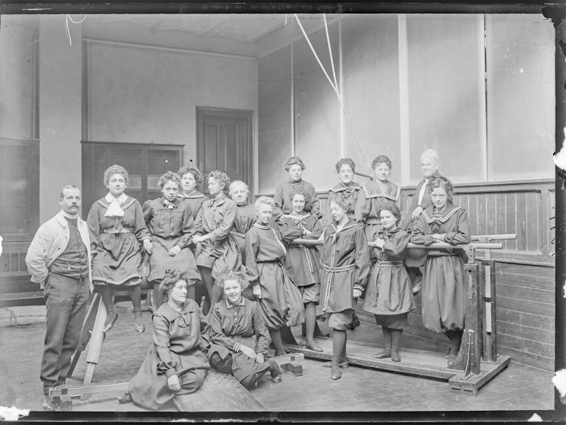 Fotografi af en gruppe kvinder iført datidens gymnastikdragt i en gymnastiksal.
