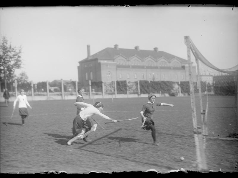 Fire kvinder spiller hockeykamp på græs