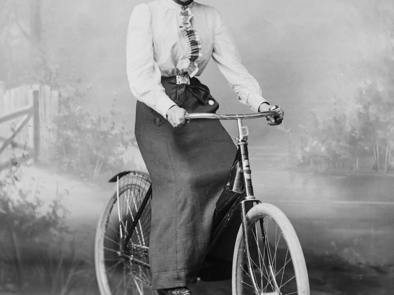 Fotografi af en kvinde i fint tøj på en cykel.