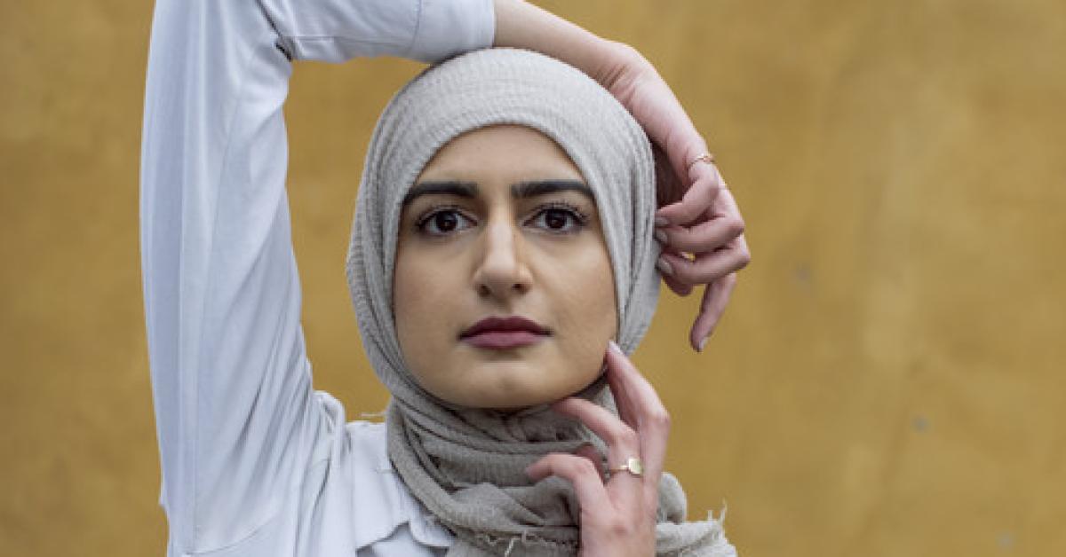 The poet Naiha Khiljee poses in white in front of an ocher yellow wall.
