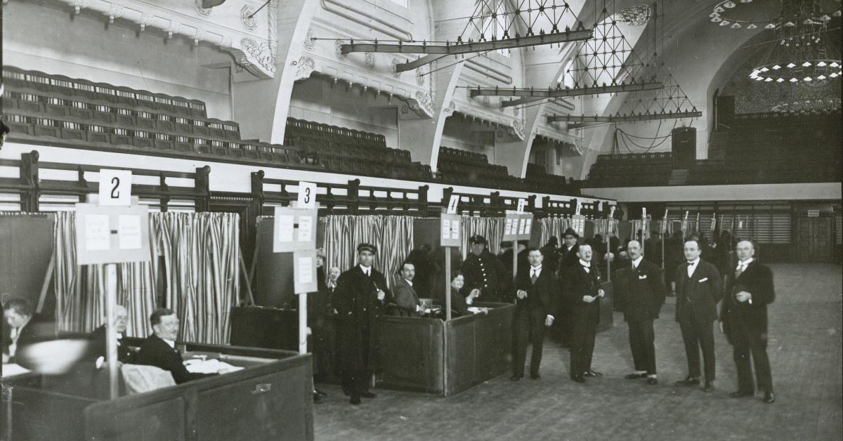 Mænd i jakkesæt står i afstemningslokale i gymnastiksal 2. dec. 1926