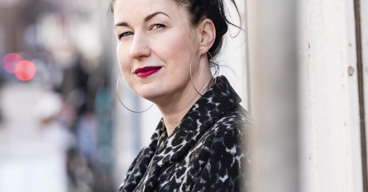 Woman with dark hair and purple lipstick looking at the camera