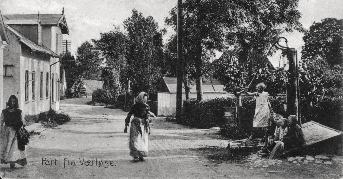 Billede af en vej, hvorpå der går to kvinder. Den ene kvinde ser ud til at tale med en anden kvinde, der står ved siden af vejen.
